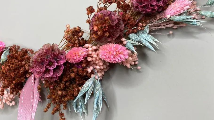 Rosa und lila Trockenblumenarrangement auf Grau.