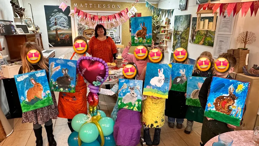 Children holding rabbit paintings at a party.