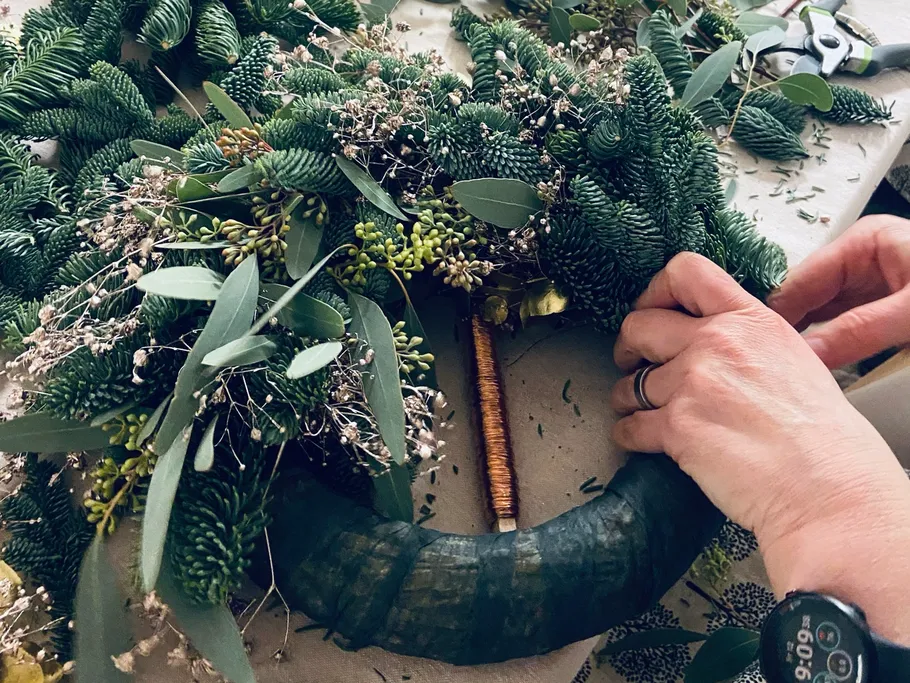 Grüner Kranz wird mit verschiedenen Pflanzen dekoriert und gestaltet.