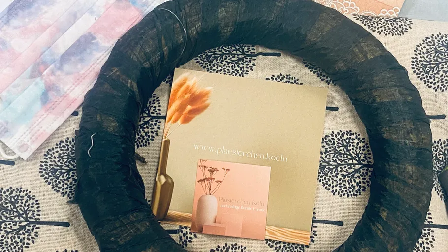 Schwarzer Kranz liegt auf gemusterter Unterlage mit Broschüre.