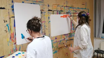 Two people painting on a colorful wall.