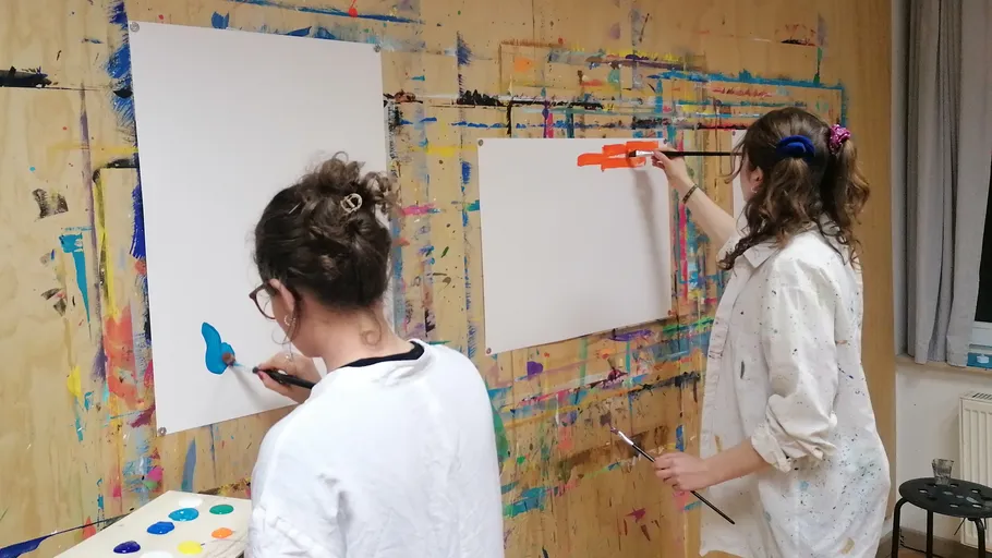 Zwei Personen malen an einer bunten Wand.