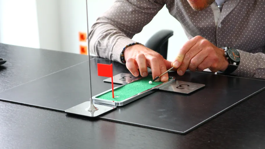 Person playing miniature golf on a desk.