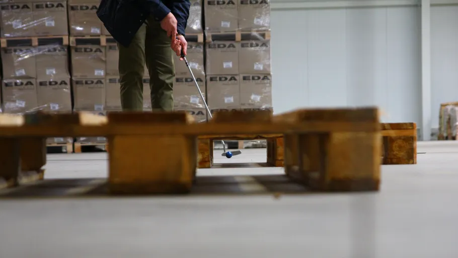 Person puttet Golfball auf Lagerhallenboden.