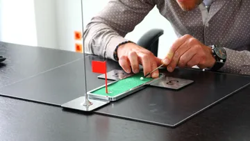 Person playing mini golf on a desk.