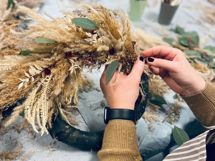 Hands make a wreath with dried plants.