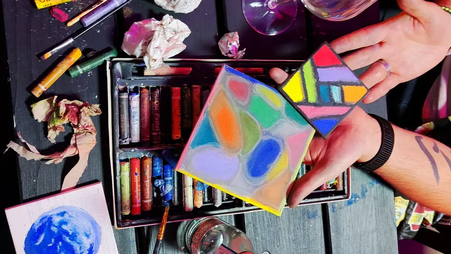 Hands holding colorful abstract art pieces.