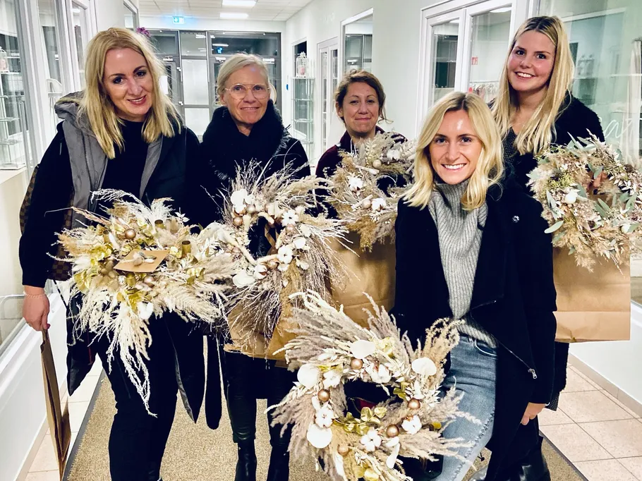 Six women hold decorative wreaths in a corridor.