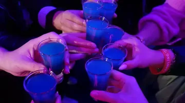 Hands holding blue shots in a toast.