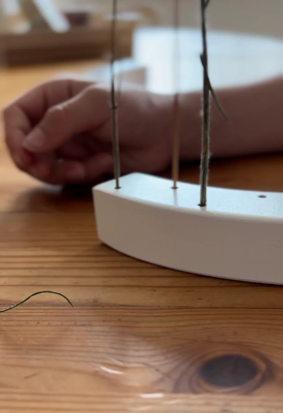 Hand touches structure with strings on table.