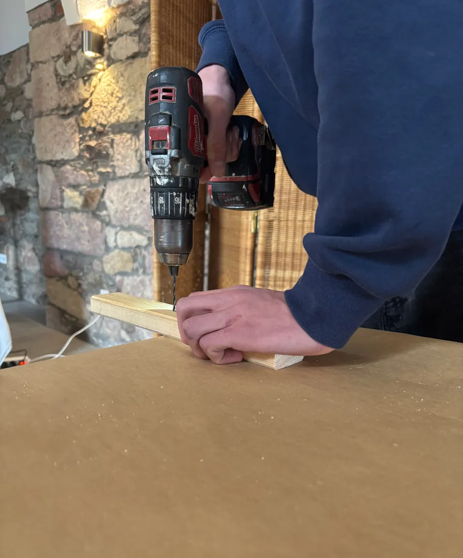 Person using drill on wooden plank indoors.