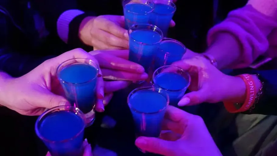 Hands holding blue shots in dim light.