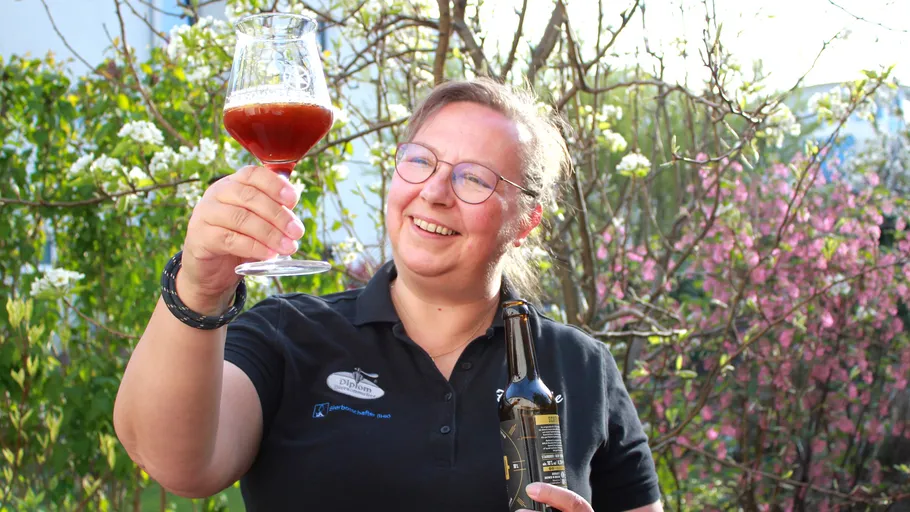 Person hält Bierglas und lächelt im Freien.
