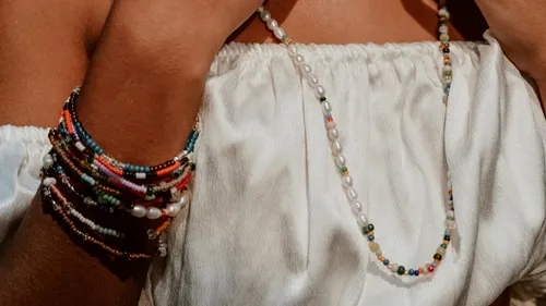 Person trägt bunte Perlenketten, weiße Bluse.