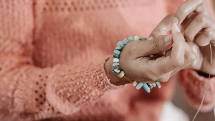 Hände fädeln Perlen auf Schnur im Innenbereich.