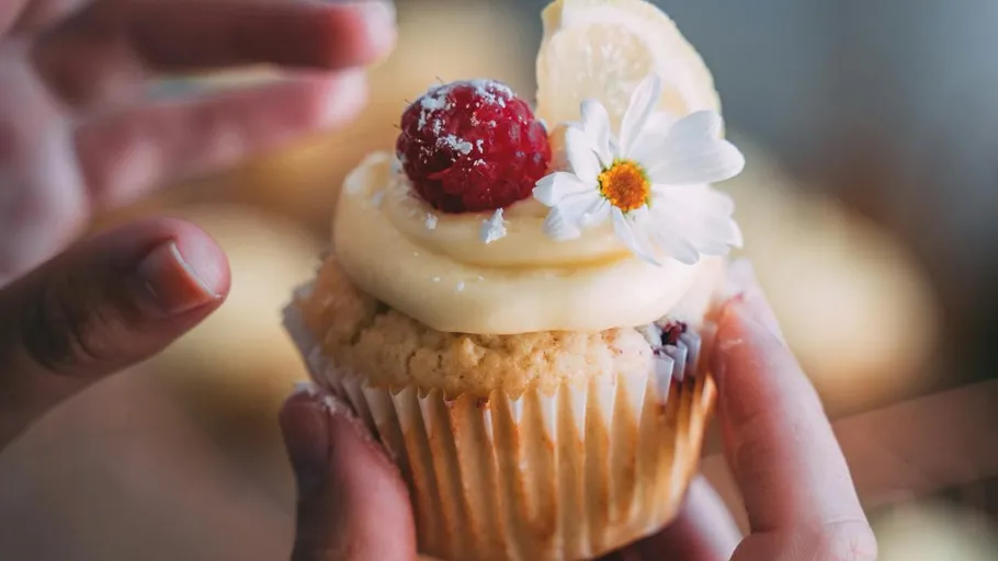 Cupcake with frosting, raspberry, and flower decoration.