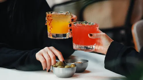 Two people toast colorful cocktails indoors.