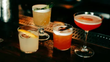 Vier Cocktails auf einer schummrigen Bar.