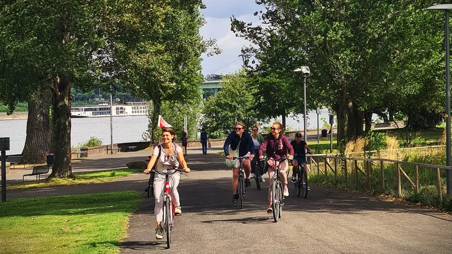 People cycling on riverside path with trees.
