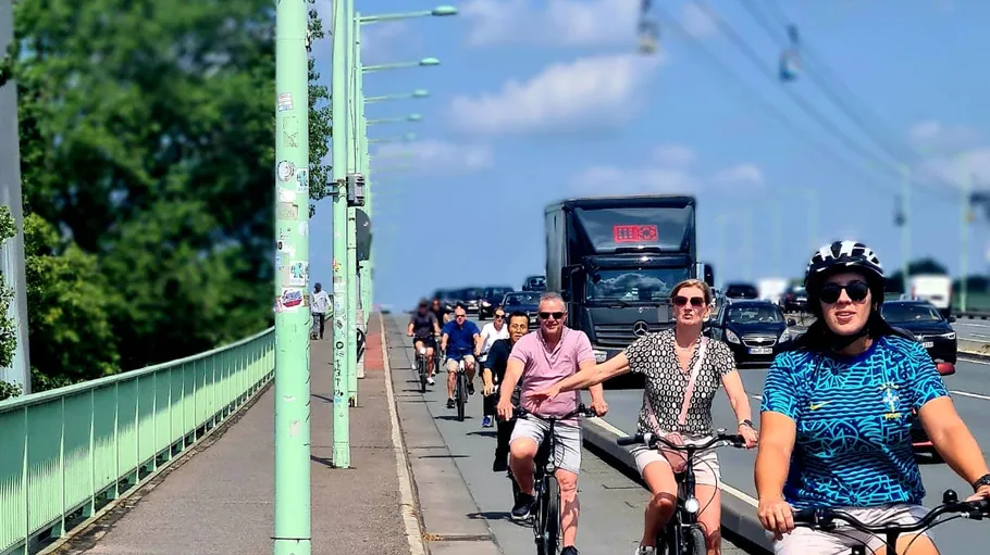 Cyclists riding on a city bridge, traffic in background.