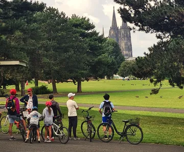 Group of cyclists in park with cathedral view.