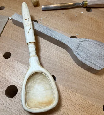 Holzlöffel mit geschnitzter Tulpe auf Werkbank.