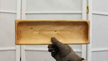 Hand hält rechteckiges Holztablett drinnen.
