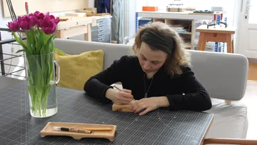 Person schnitzt Holz an einem Tisch mit Tulpen.
