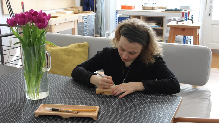 Person carving wood at table with tulips.
