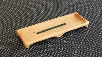Wooden tray with pencil on checkered surface.