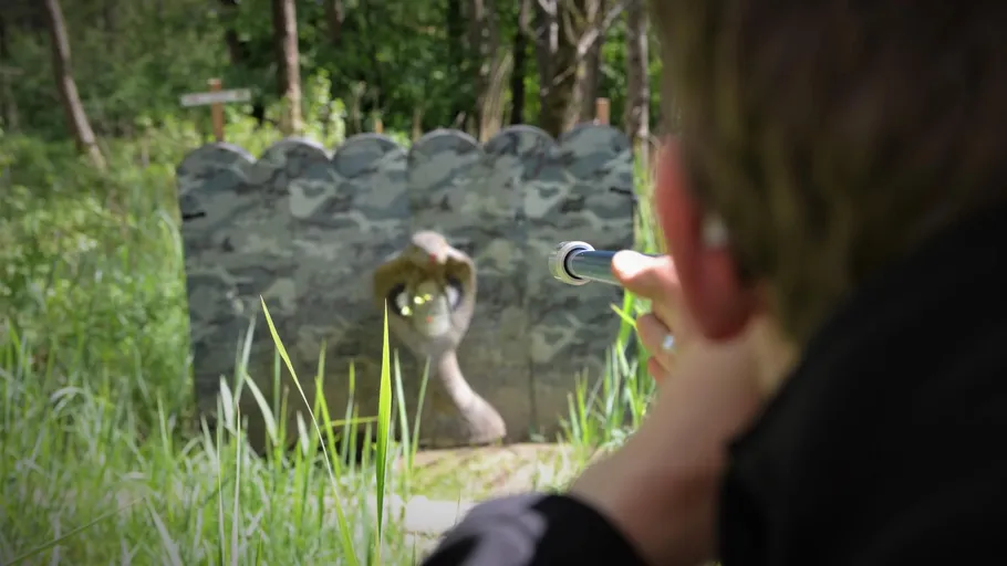 Person aiming blowgun at snake target outdoors.