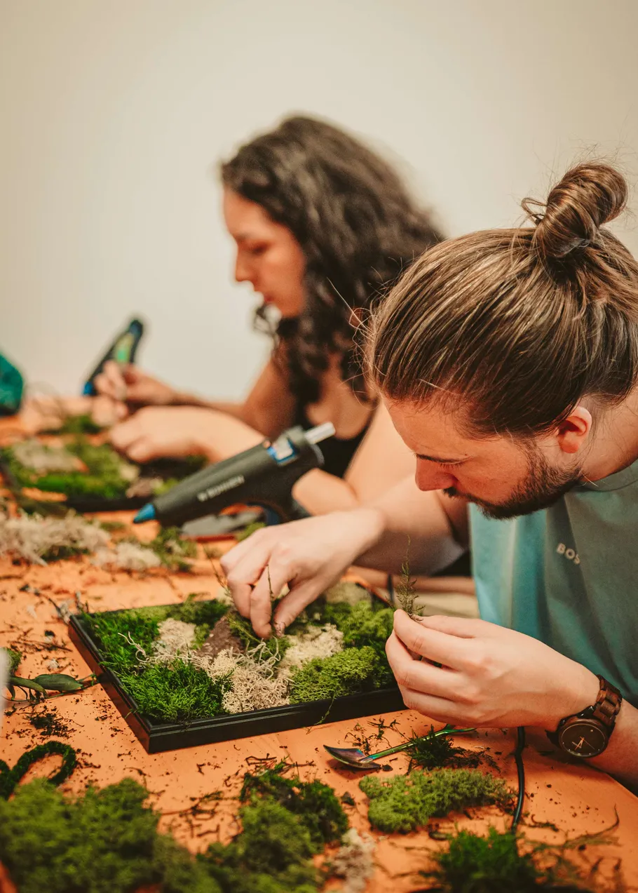 Two people crafting with moss on frames.