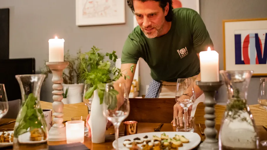 Mann deckt Esstisch mit Kerzen und Essen.