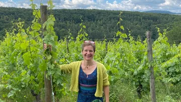 Person lächelt in einem üppigen Weinberg.