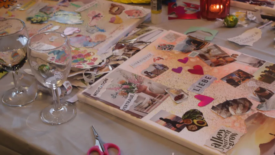 Tisch mit Collage, Schere und Weingläsern.