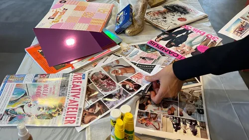 Hand holding magazine clippings on cluttered table.