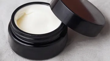 Dose mit Creme, offener Deckel auf Stoff.