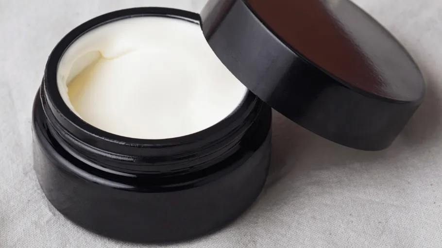 Jar of cream with open lid on fabric.