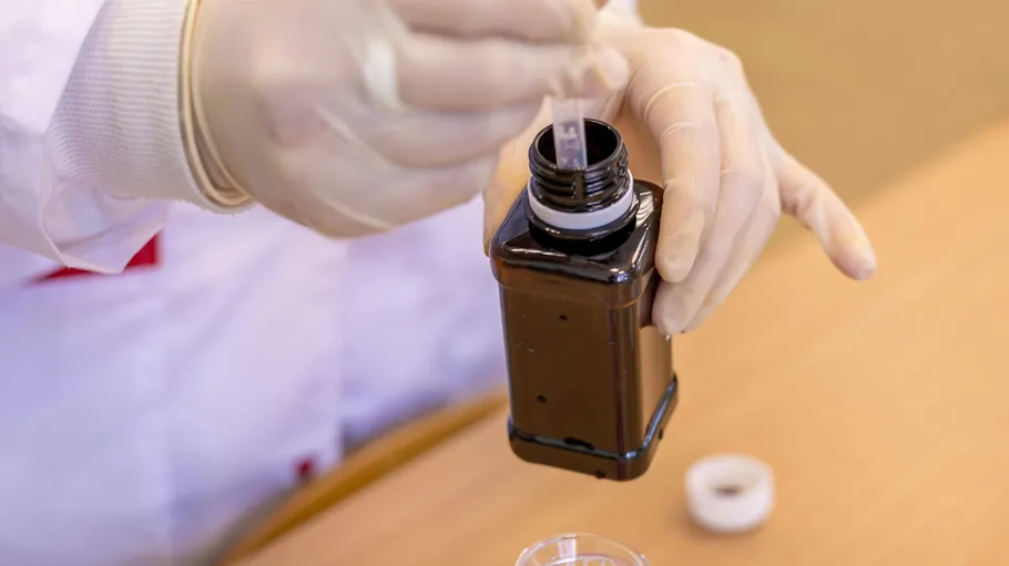 Person wearing gloves handling a dark bottle.