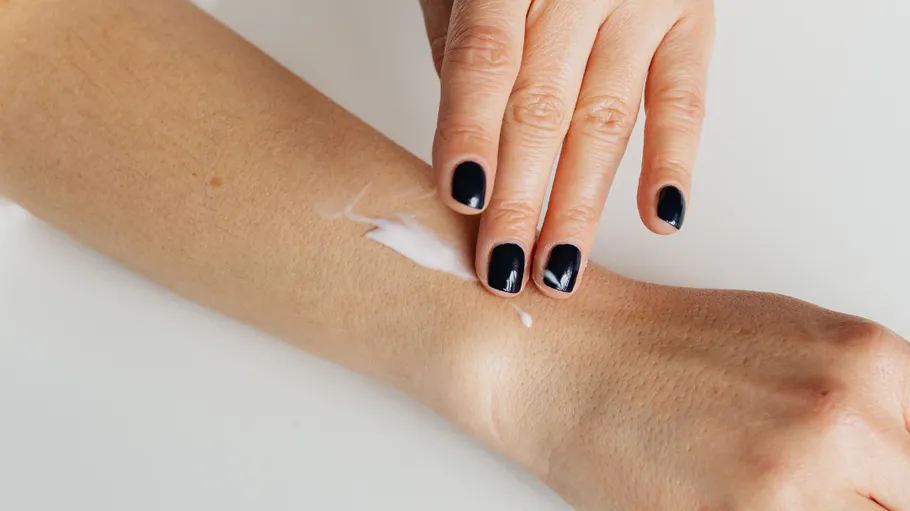 Hand trägt Lotion auf Unterarm auf, drinnen.