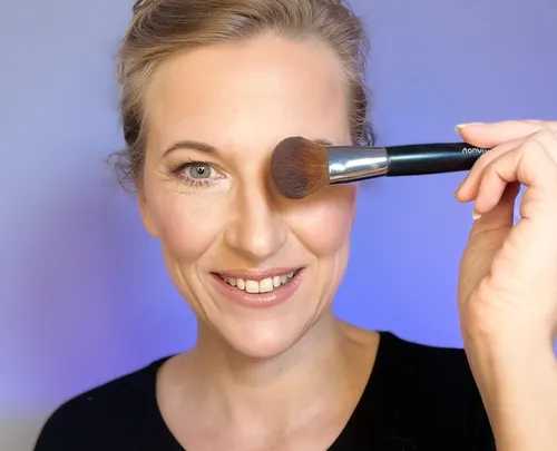 Smiling woman holding makeup brush by face.