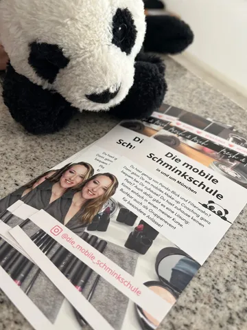 Panda plush toy next to makeup school brochure.