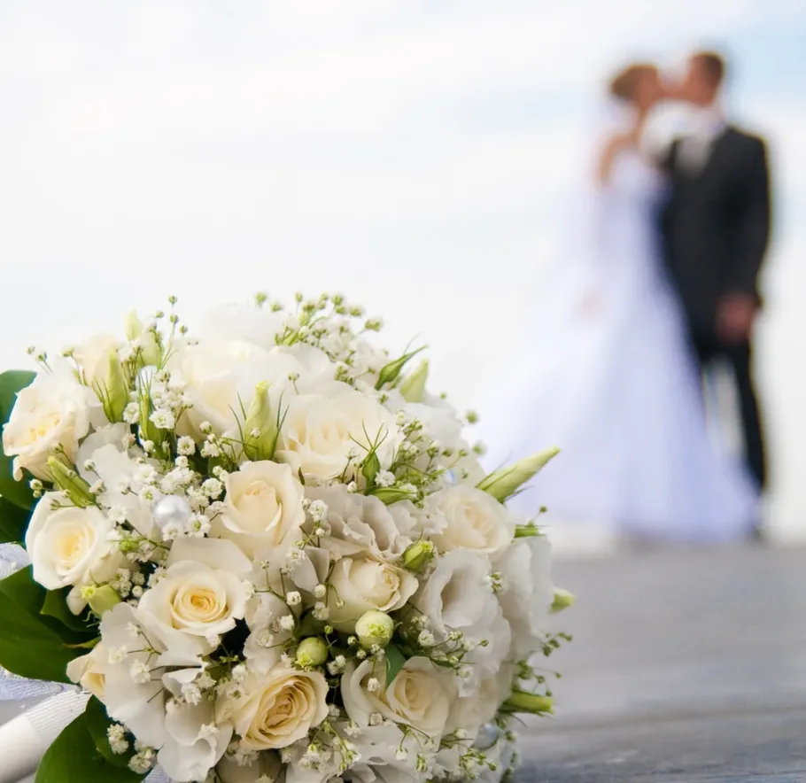 White roses bouquet, blurred couple in background.