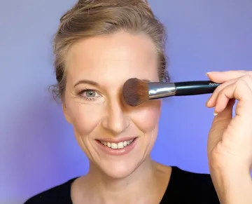 Woman smiling, holding makeup brush near face.