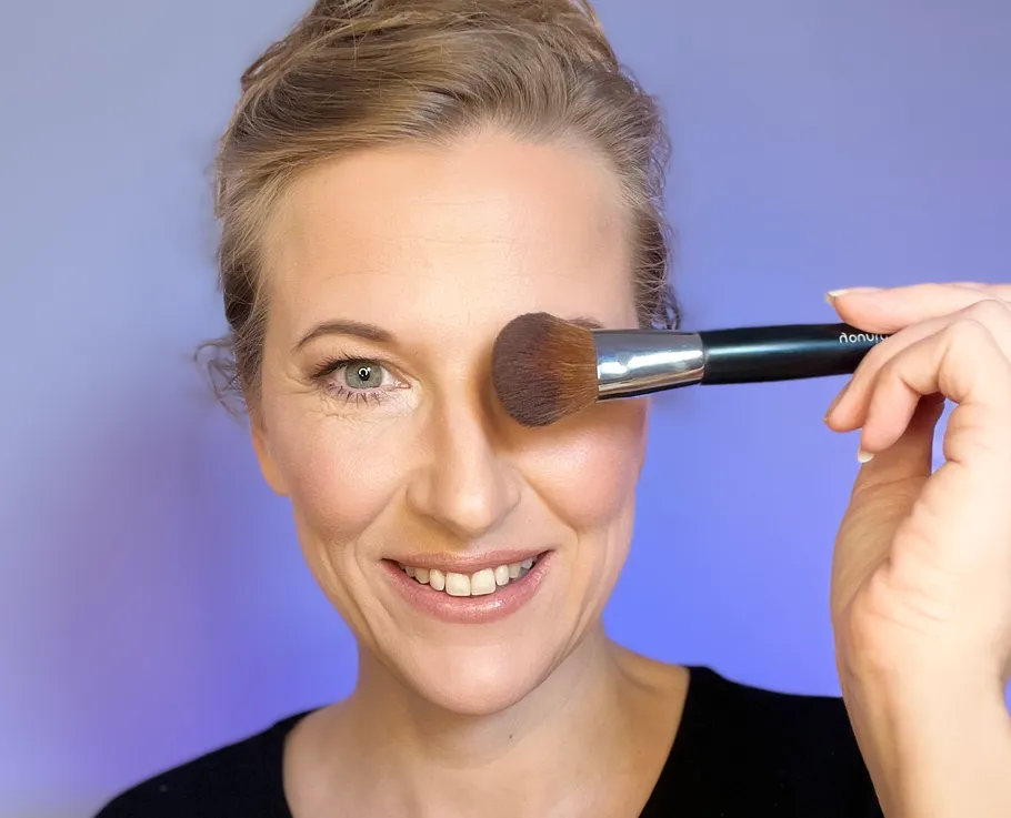 Woman smiling, holding makeup brush near face.