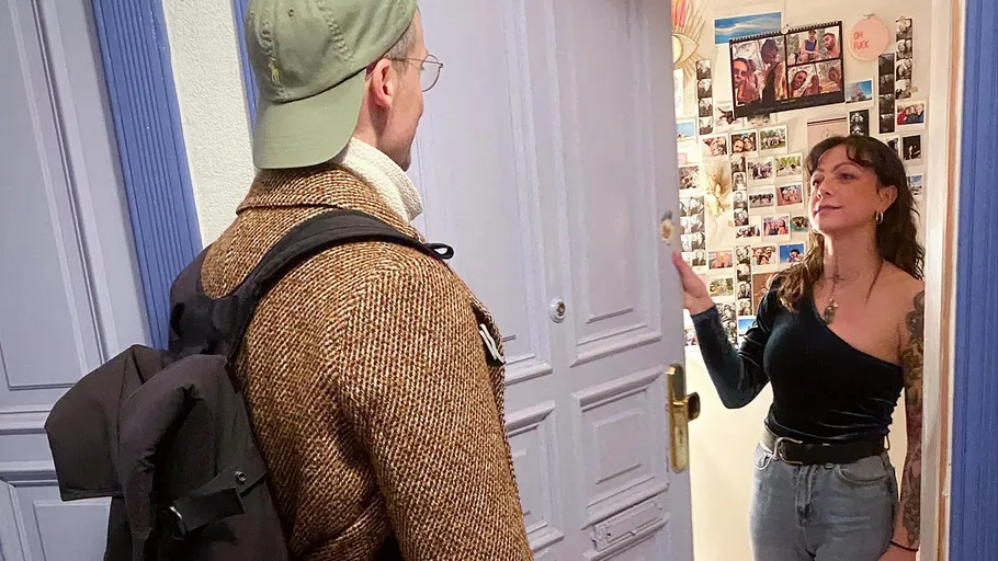 Frau öffnet Tür für Mann mit Rucksack innen.