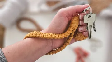 Hand hält Schlüssel mit Makramee-Schlüsselanhänger.