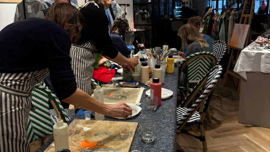 Menschen malen an einem Workshop-Tisch drinnen.