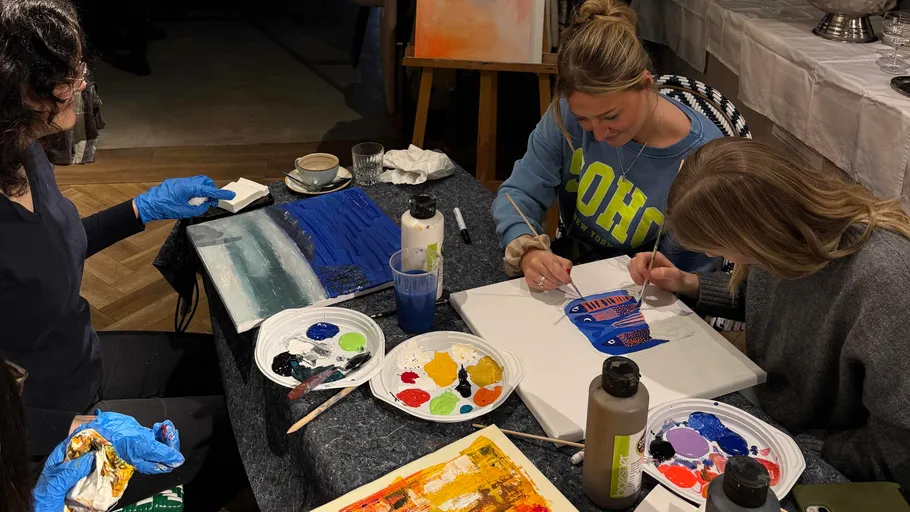 Three women painting at a table indoors.