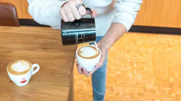 Person gießt Latte-Art in Kaffeetasse.